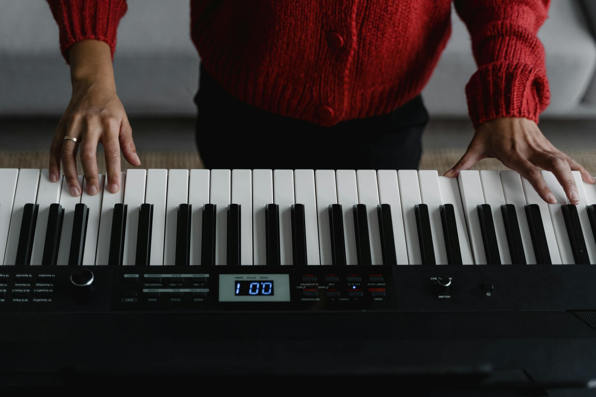 Person wearing red cardigan plays a digital piano indoors.